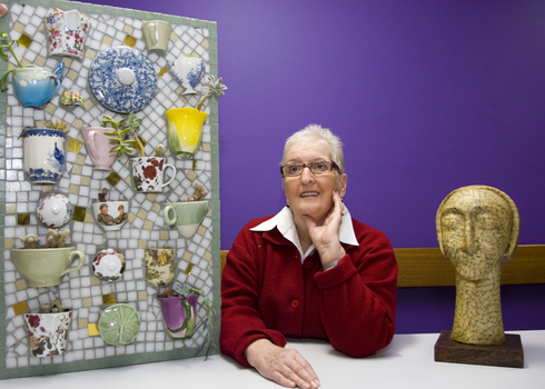Woman with sculpture of head on long neck and mosaic of teacups