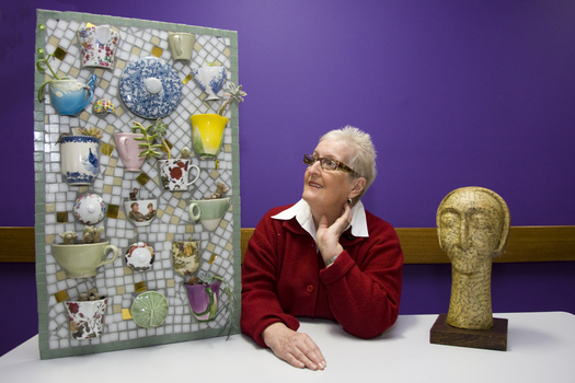 Woman with sculpture of head on long neck and mosaic of teacups
