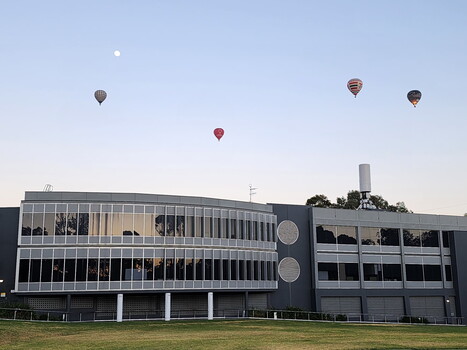 Four hot air balloons and the moon above the Kooyong building