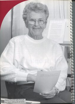 Clarys Churchill beside her desk with printed pages in her hand