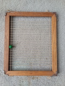 Wooden frame with elastic stretched across frame and string with bead on left side