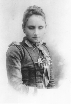 Young adult female in studio portrait wearing collared, long sleeved dress with fuchsia necklace