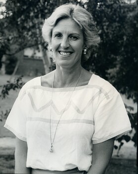 Woman stands smiling for camera wearing pleated skirt with white top with zig zag across torso