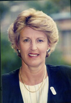 Woman in blue jacket, striped blouse, gold curb chain necklace, round earrings and elongated oval badge