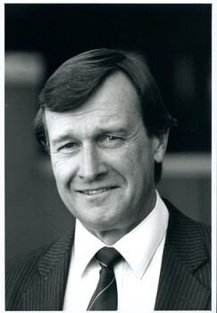 Man in pinstripe suit, light coloured shirt and striped tie standing outside a building