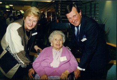 Male and female stand either side of an elderly female in a wheelchair