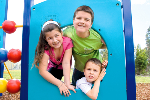 Three Law children putting their head through an opening at a playground