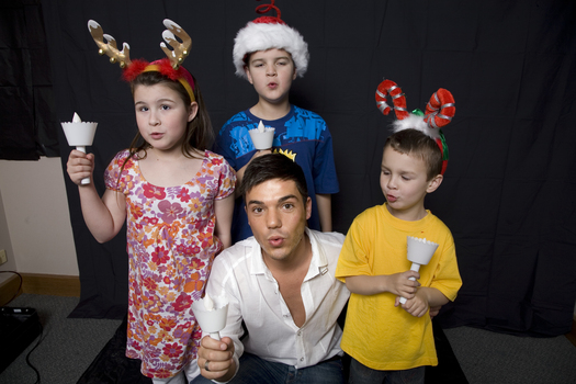 Kate, Nicholas and Jacob Law with Anthony Callea holding candles and wearing Christmas hats