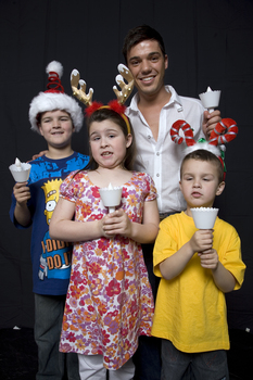 Kate, Nicholas and Jacob Law with Anthony Callea holding candles and wearing Christmas hats