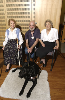 Two seated women in the Kooyong Day Centre with their walking sticks with Colin Pascoe and his dog