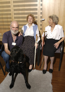 Two seated women in the Kooyong Day Centre with their walking sticks with Colin Pascoe and his dog