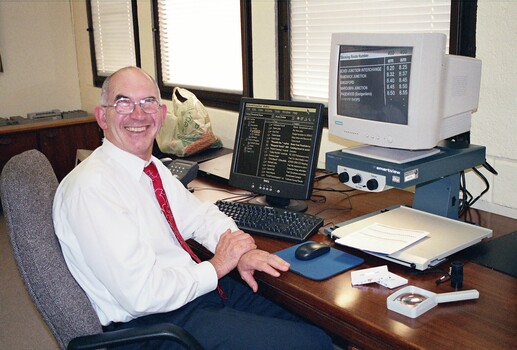 John Landau sitting at his desk with his computer and screen magnifier