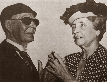 Helen Keller finger spelling with an elderly man wearing dark glasses