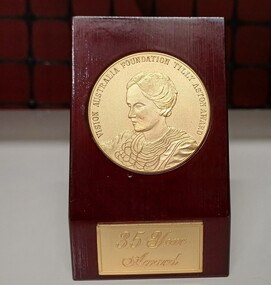 Gold toned medal inlaid into red coloured wood block