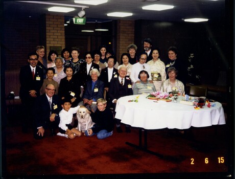 Large group of people sitting or standing next to covered table