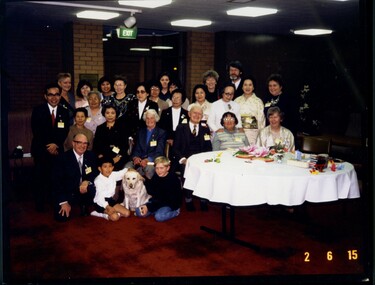 Large group of people sitting or standing next to covered table