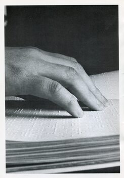 Hands reading a Braille page against dark background