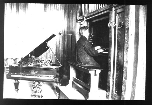 Male playing the organ with a piano behind him