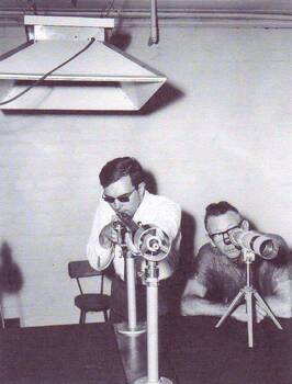 Coach Alley looks through a telescope whilst a shooter lines up the sight