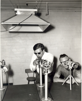 Coach Alley looks through a telescope whilst a shooter lines up the sight