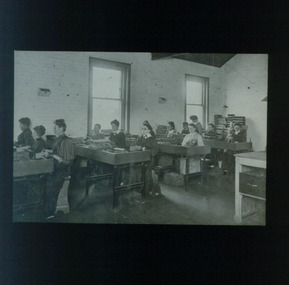 12 female workers sit at benches with items before them