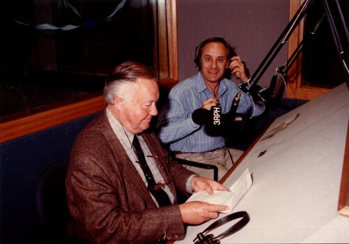 Bud Tingwell sits at the presenters desk with an announcer beside him