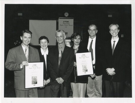 Group of six people holding two awards