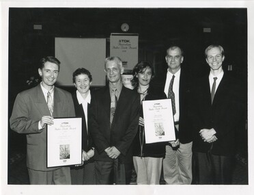 Group of six people holding two awards