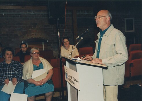 Presenter at podium with Rebecca Maxwell in the audience