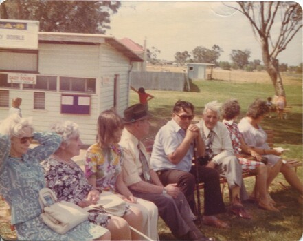 Group of people seated on chairs outside a track TAB