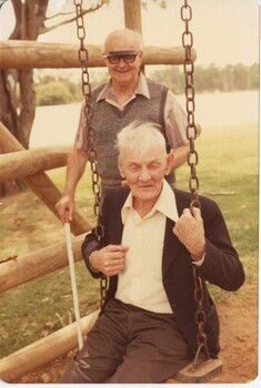 Elderly man on swing with another man standing behind him