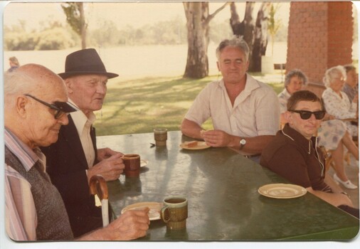 Four men sit around a table with cups of tea