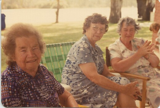 Three women in folding chairs beside the lake
