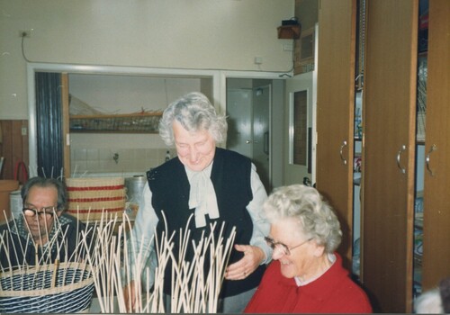 Two people weave baskets whilst another observes