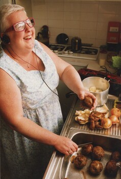 Women wearing headphones as she scrubs potatoes in the kitchen