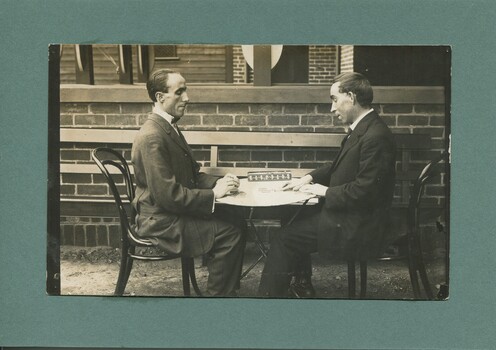 Two men sit playing dominoes outside the Braille Library