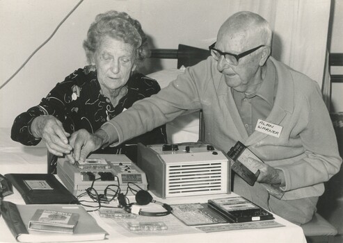 Two older people with a table showing audio books and players