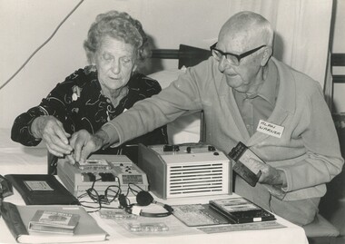Two older people with a table showing audio books and players