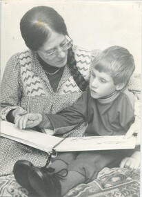 Woman sits next to boy, guiding his hand