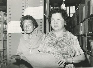 Two older women, one holding an open Braille book