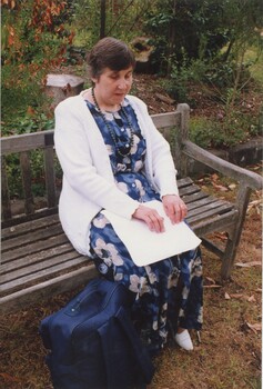 Carol McGowan sitting on a garden bench reading a page of Braille
