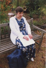 Carol McGowan sitting on a garden bench reading a page of Braille