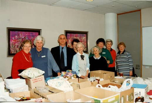 Man stands amongst a group of woman with boxes piled in front of them
