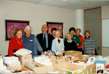 Man stands amongst a group of woman with boxes piled in front of them
