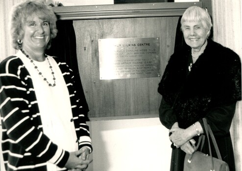 Two women stand either side of a plaque