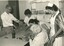 Nursing staff and visitors look at handicrafts as women threads machine