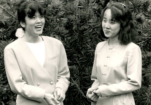 Two Japanese women stand next to a bush