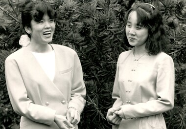 Two Japanese women stand next to a bush