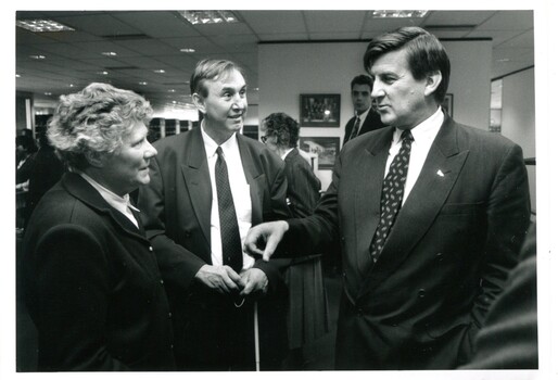 Two men and one woman chat in a busy room