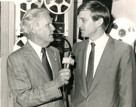 Arthur Wilkins holds a microphone as he speaks to Jeff Kennett with magnetic reels in the background